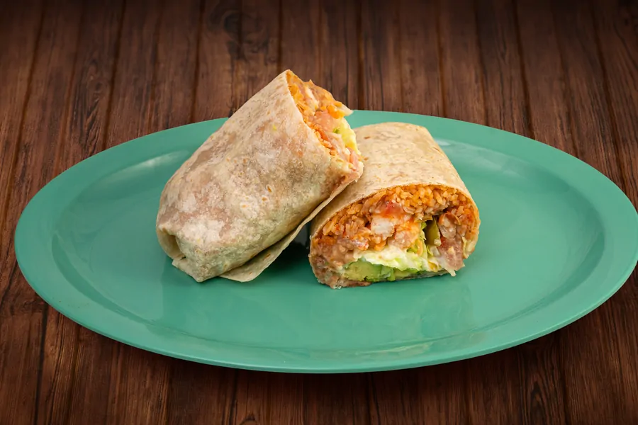 A burrito cut in half on a teal plate, the cut face showing rice, beans, meat, avocado and cheese.
