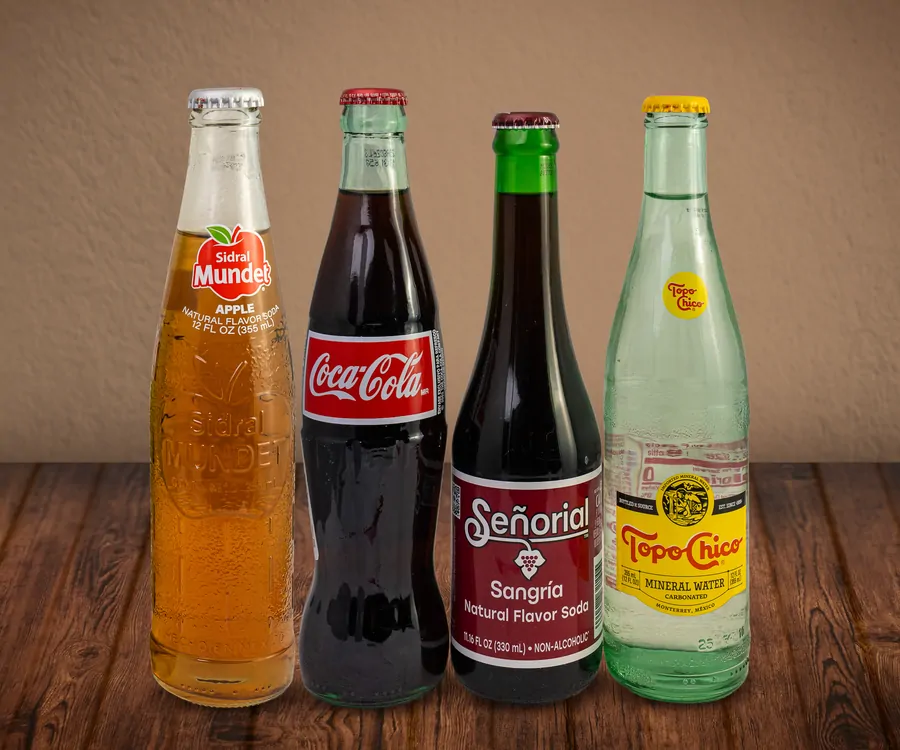 Four glass bottles together: Sidral Mundet apple soda, Coca-Cola, Señorial sangria soda and Topo Chico mineral water.