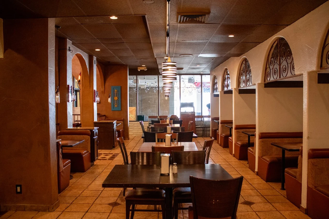 The dining room looking down the middle, tile floor and pendant lamps overhead, wooden booths along both walls and the carved archways on the right.